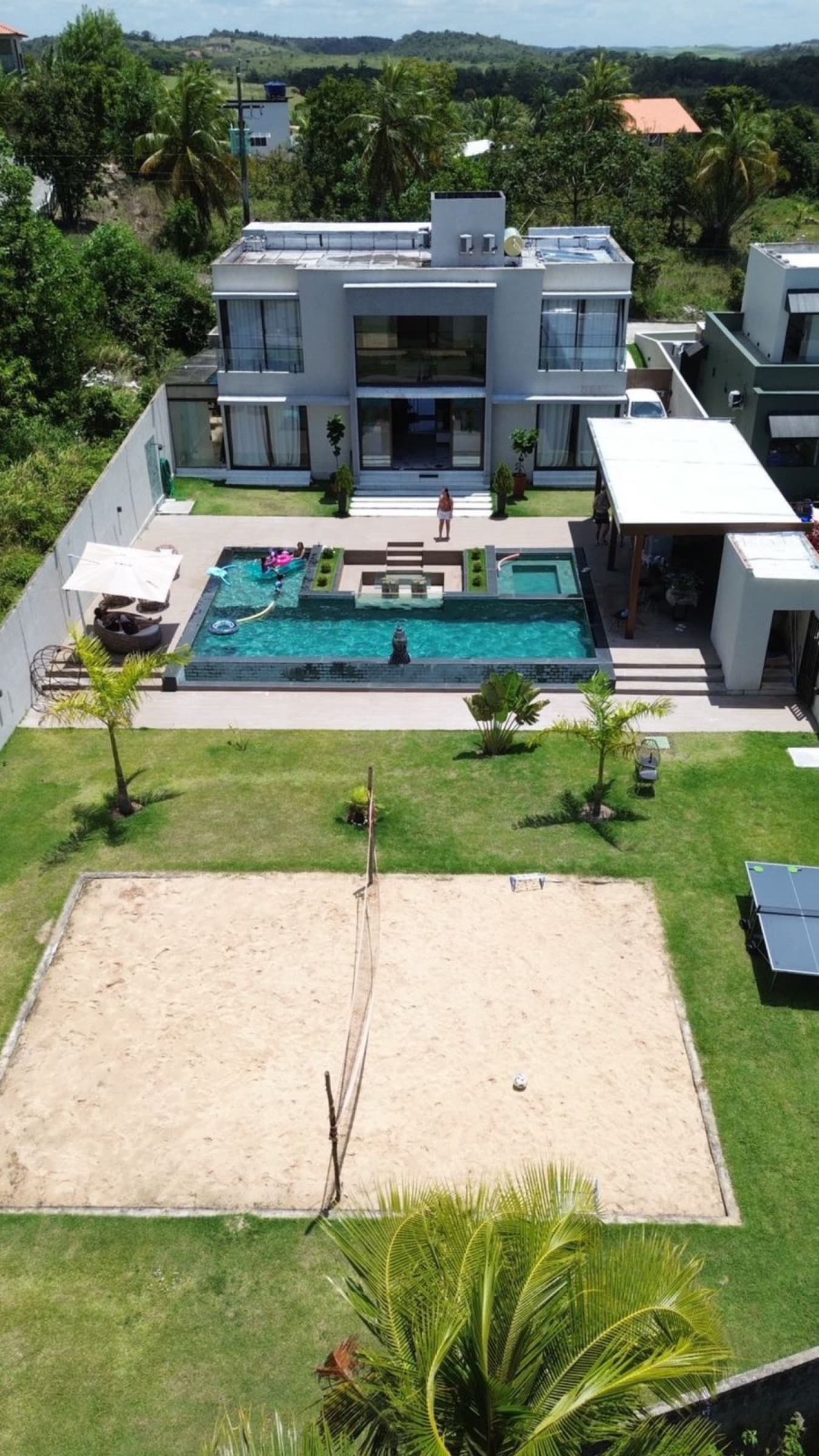 Vista aérea da Luxo Oásis, mostrando a casa, a piscina e a quadra de vôlei de praia