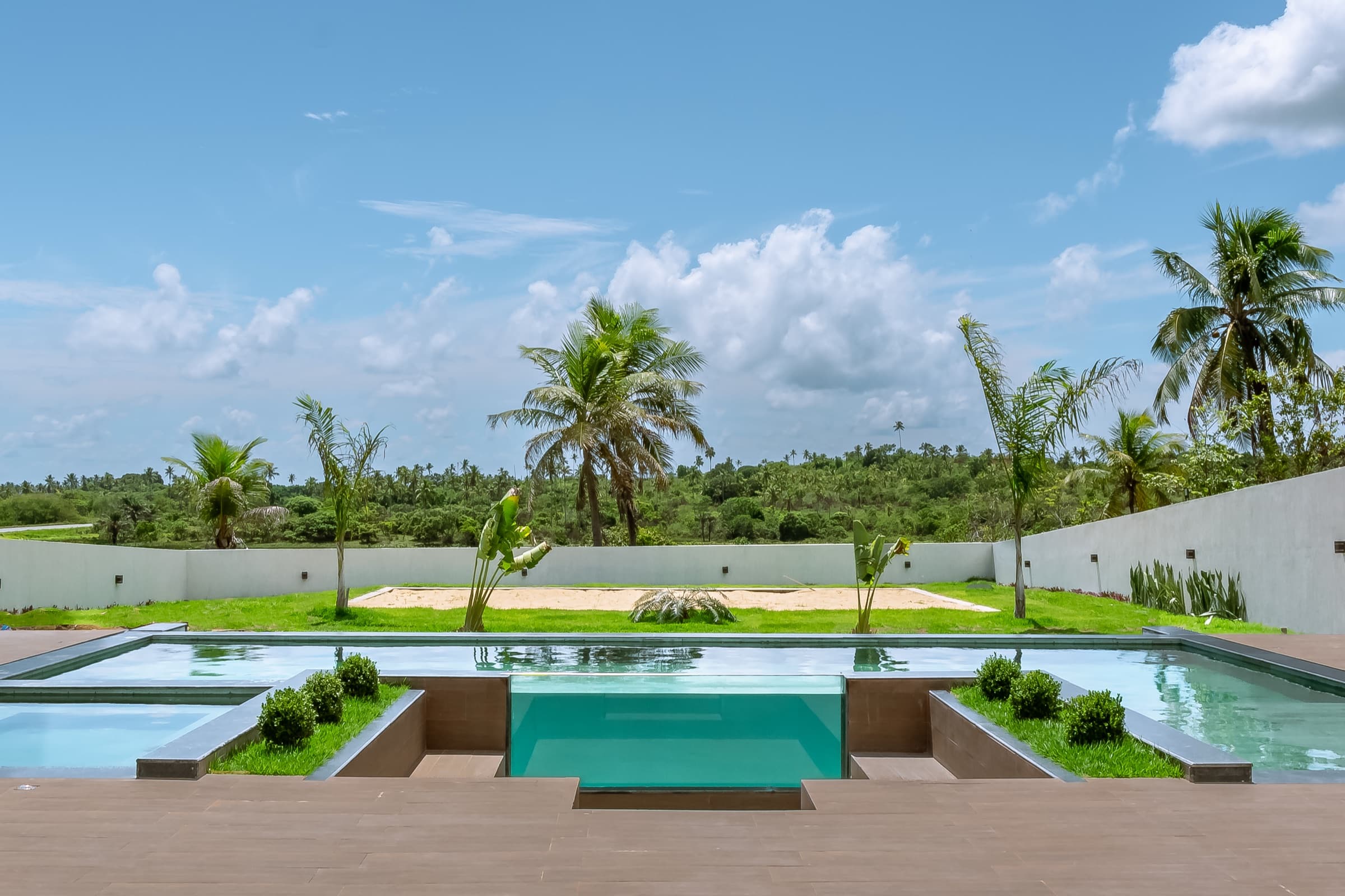 Piscina com borda de vidro e jardim tropical da Luxo Oásis